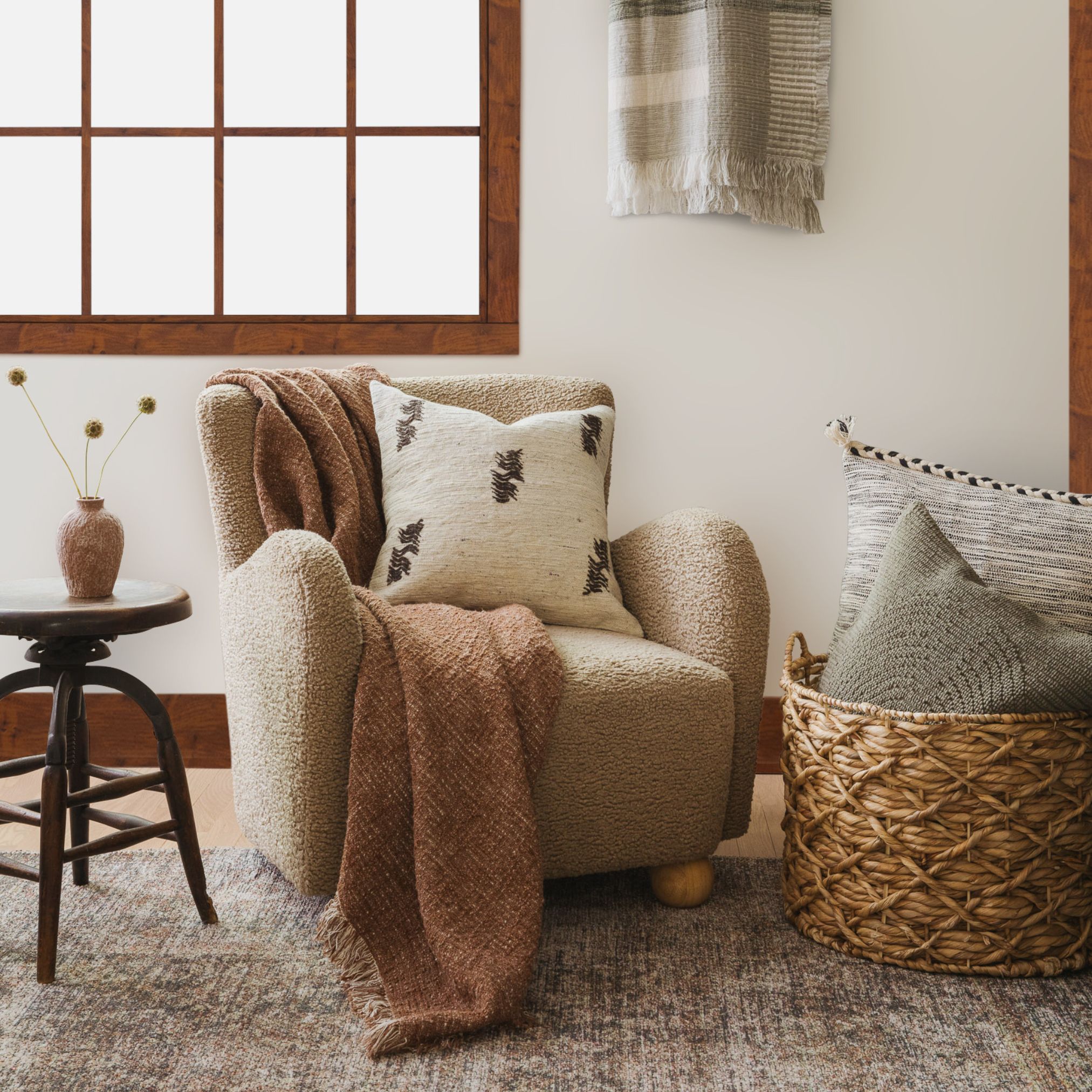 Brown leather sectional with assorted neutral throw pillows, woven basket, and beige blanket on a terracotta tile rug.