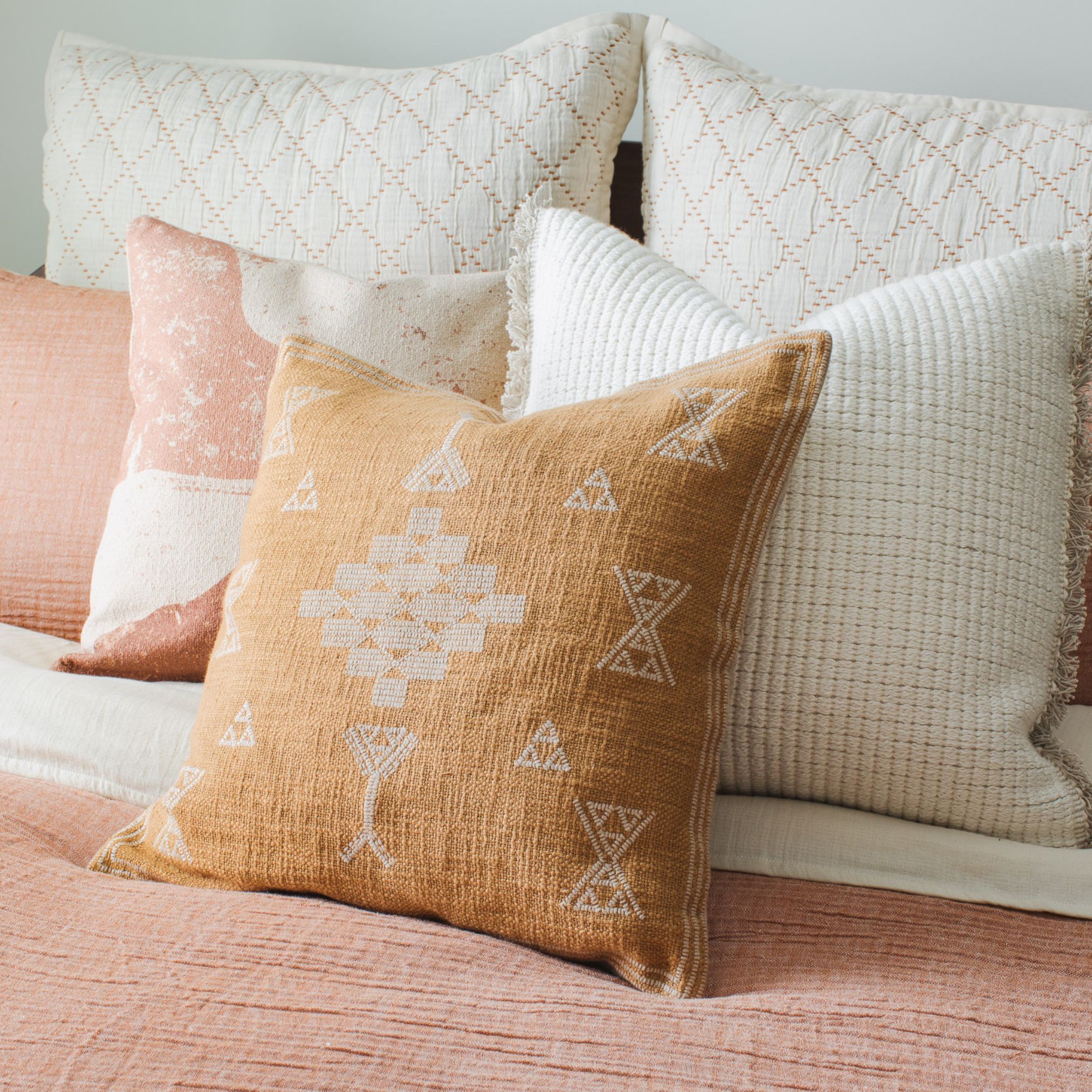 10 Burnt orange decorative pillow with white embroidery on a pink bed with white accent pillows