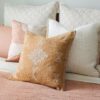 Burnt orange decorative pillow with white embroidery on a pink bed with white accent pillows