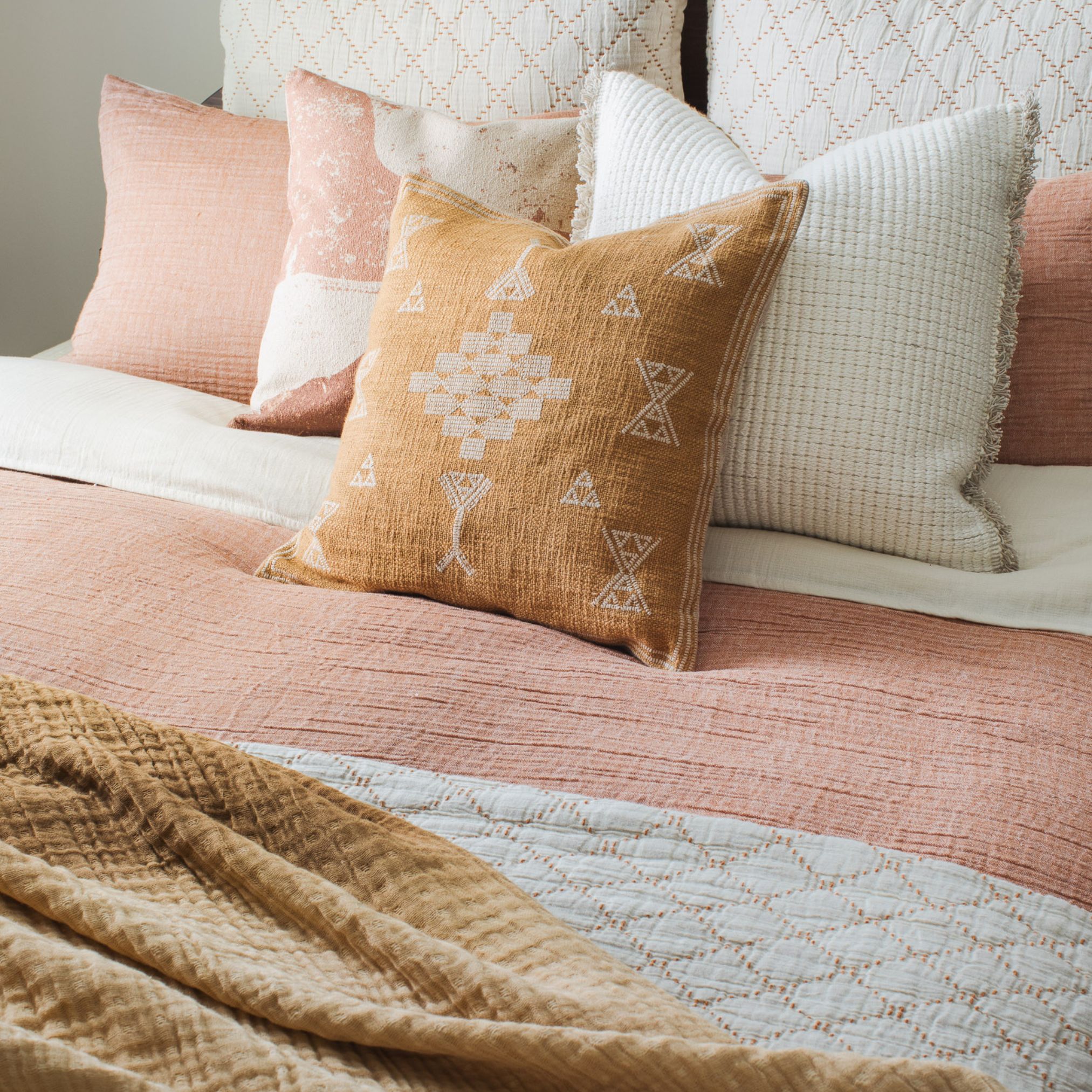 Burnt orange decorative pillow with white embroidery on a pink bed with white accent pillows