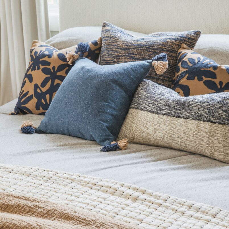 Bed with blue and beige pillows, a botanical-patterned pillow, and a striped duvet cover