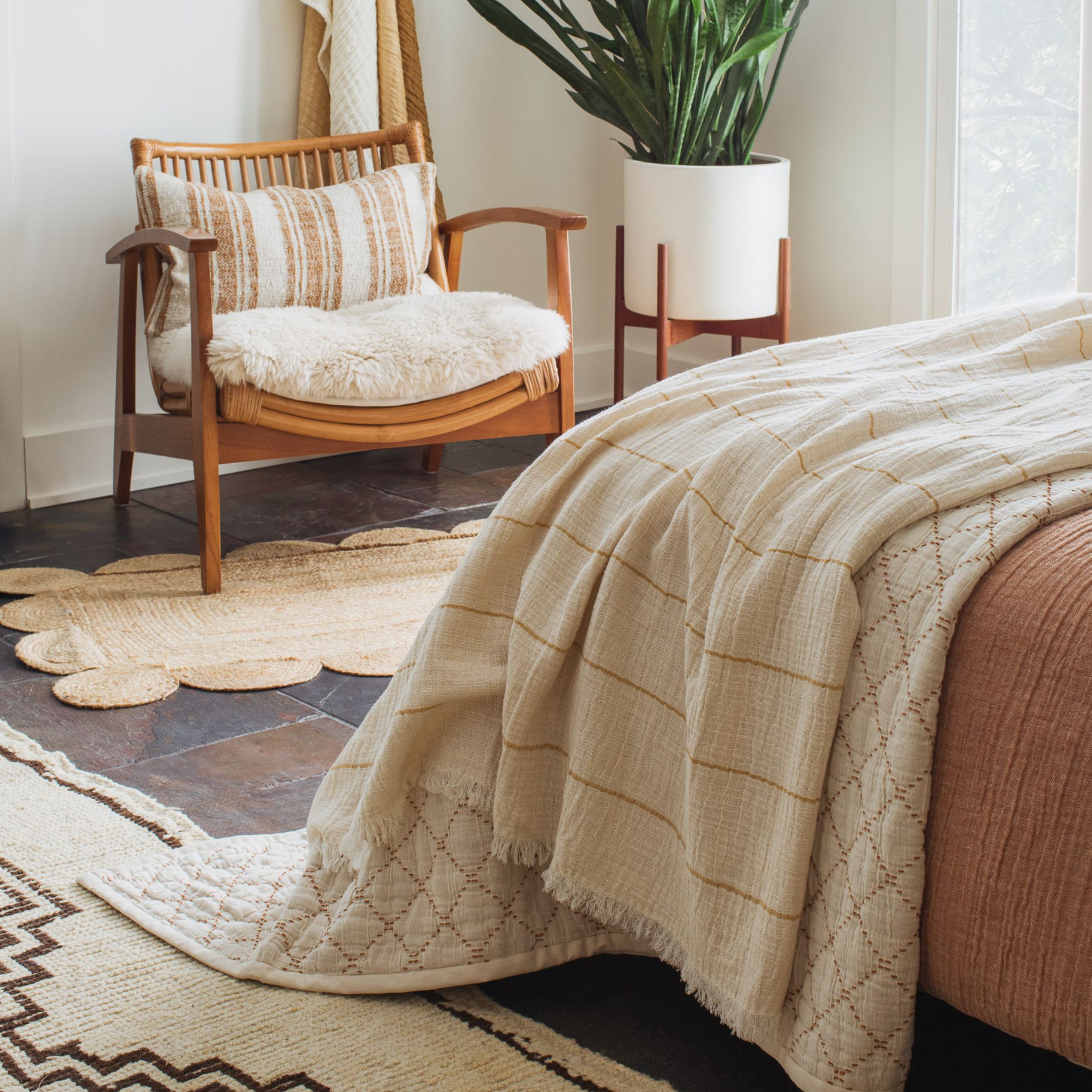 Bed with beige and rust bedding, layered pillows, and a nightstand with decor and a plant