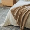 Beige and rust throw blankets draped over the foot of a bed with a light gray rug underneath
