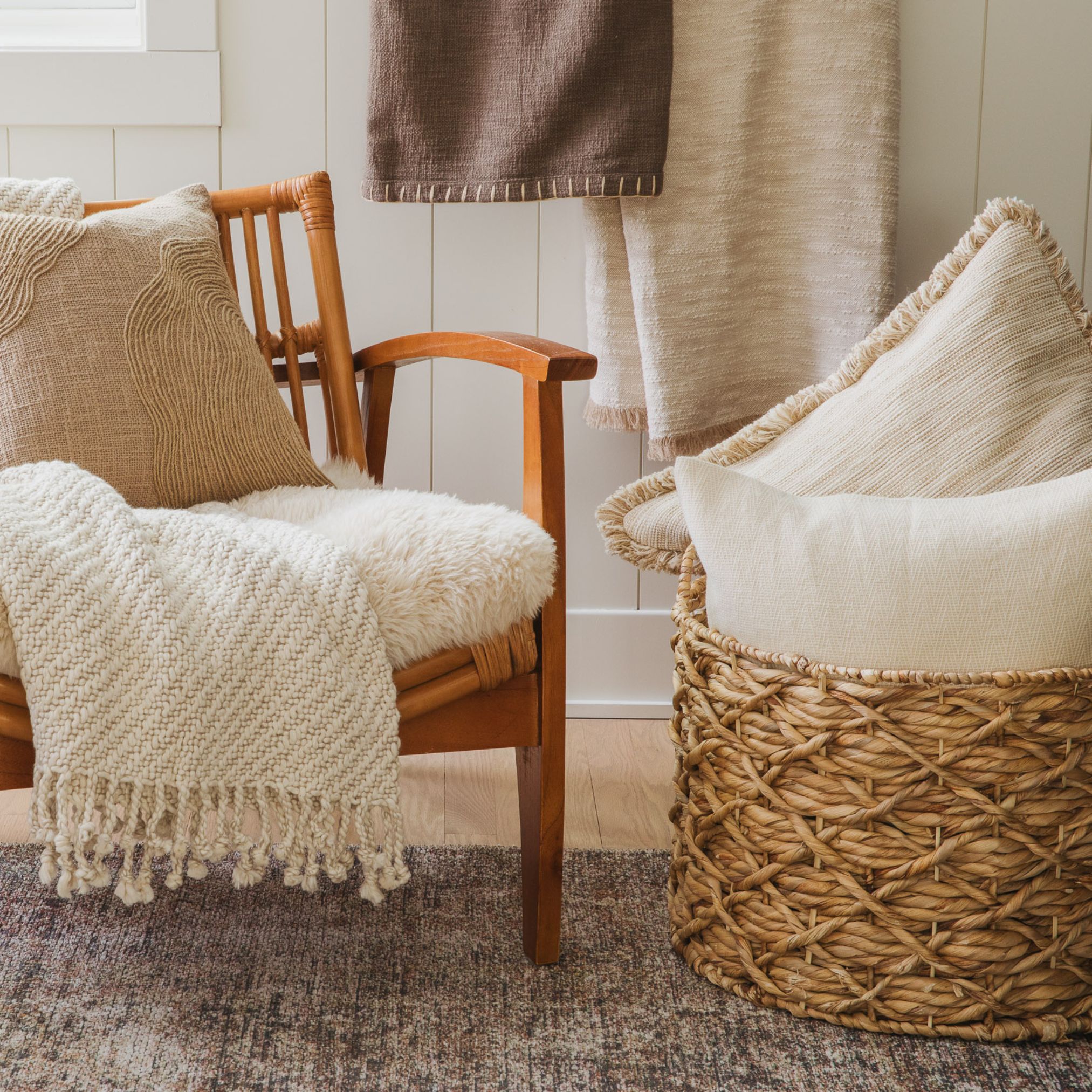 Neutral-toned room with a white cushioned chair, woven basket, and soft blankets on a textured rug