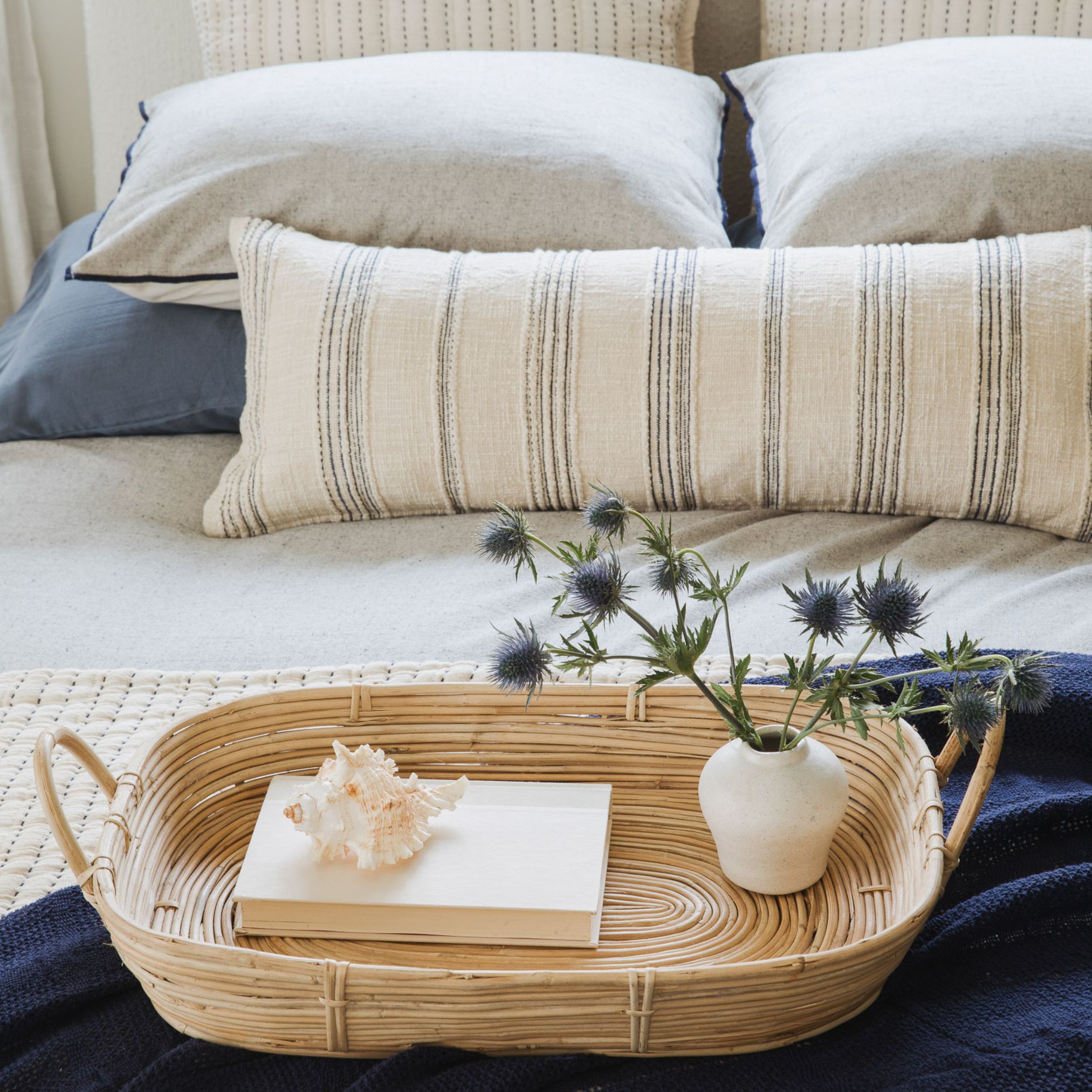 Folded navy blanket and neutral throw pillows arranged in a basket at the foot of a bed