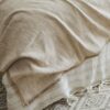 Close-up of a beige woven blanket with soft folds and fringed edges