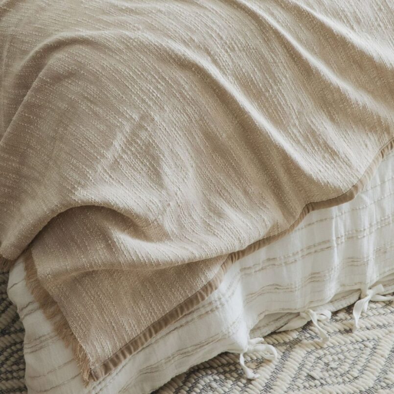 Close-up of a beige woven blanket with soft folds and fringed edges