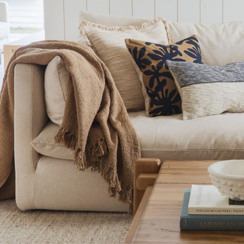 Beige sofa with layered neutral pillows and a rust-colored throw draped over the arm