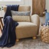 Light tan armchair with a navy blue throw and neutral pillows on a textured rug in a cozy room