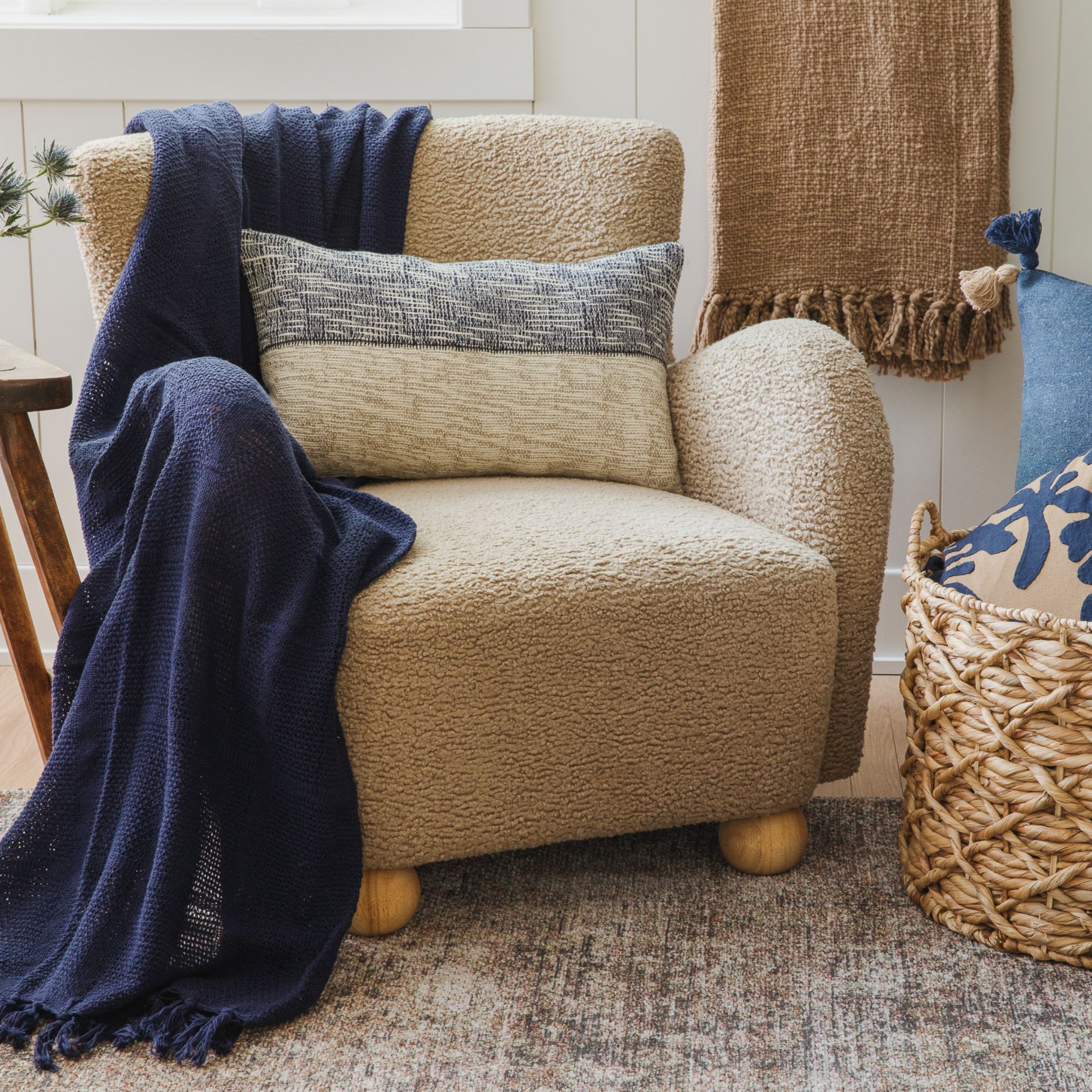 Light tan armchair with a navy blue throw and neutral pillows on a textured rug in a cozy room