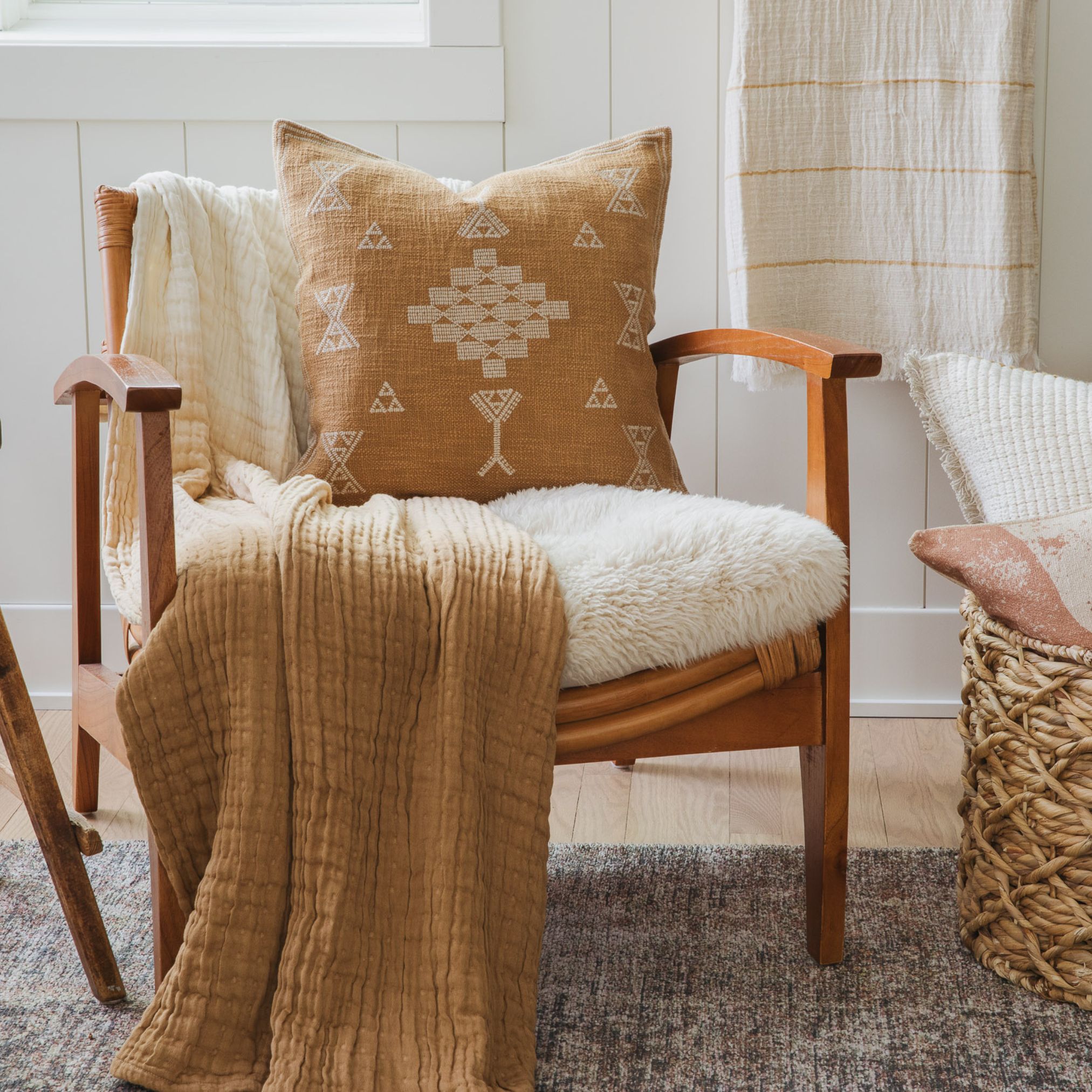 Neutral-toned room with a white cushioned chair, woven basket, and soft blankets on a textured rug