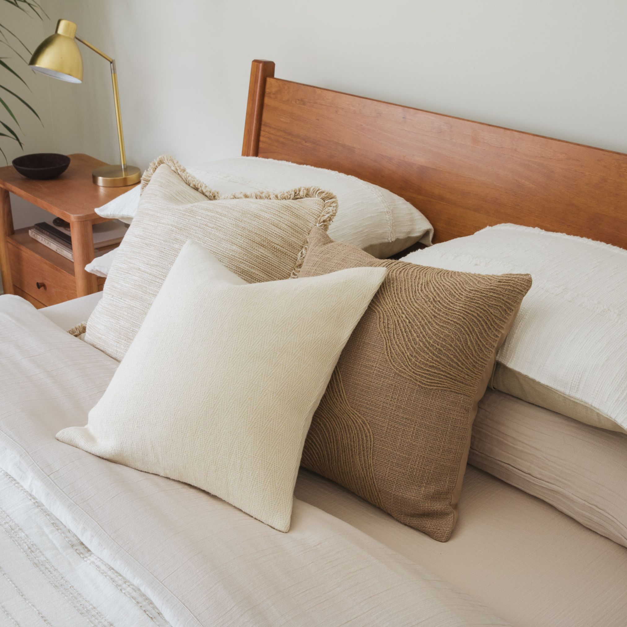 Bed with light beige sheets, white and tan pillows, and a wood headboard