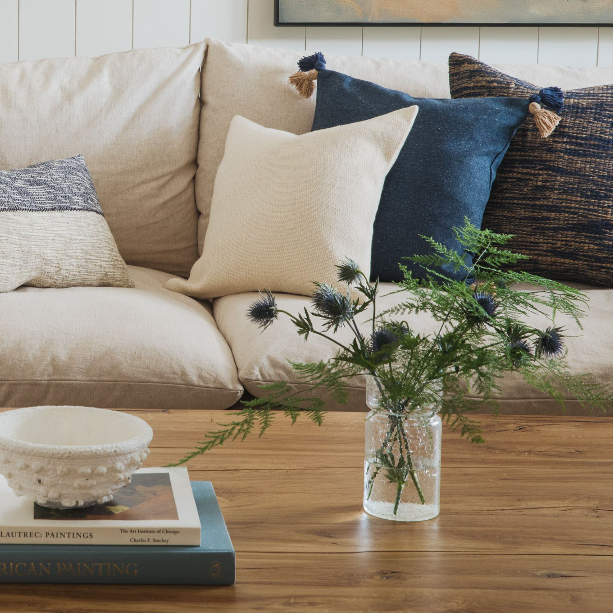 Light beige sofa with blue and green accent pillows and a glass coffee table
