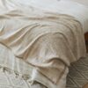 Close-up of a beige woven blanket with soft folds and fringed edges