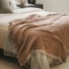 Close-up of a rust woven blanket with soft folds and fringed edges