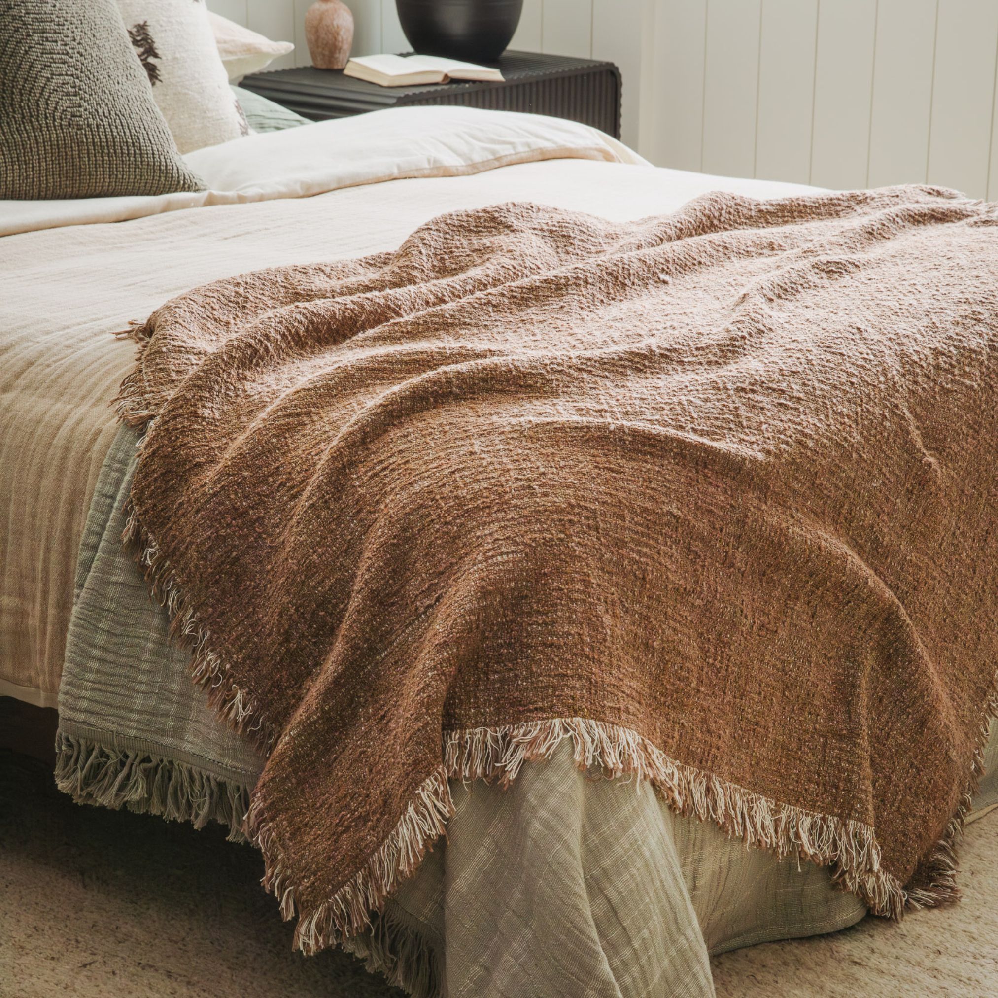 Close-up of a rust woven blanket with soft folds and fringed edges