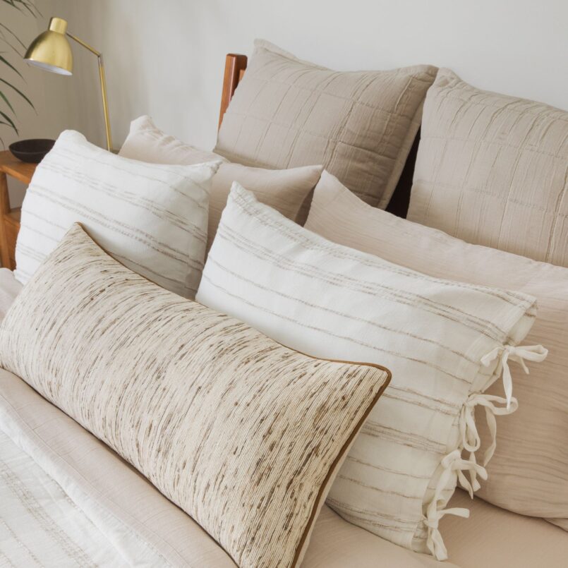 Bed with light beige sheets, white and tan pillows, and a wood headboard