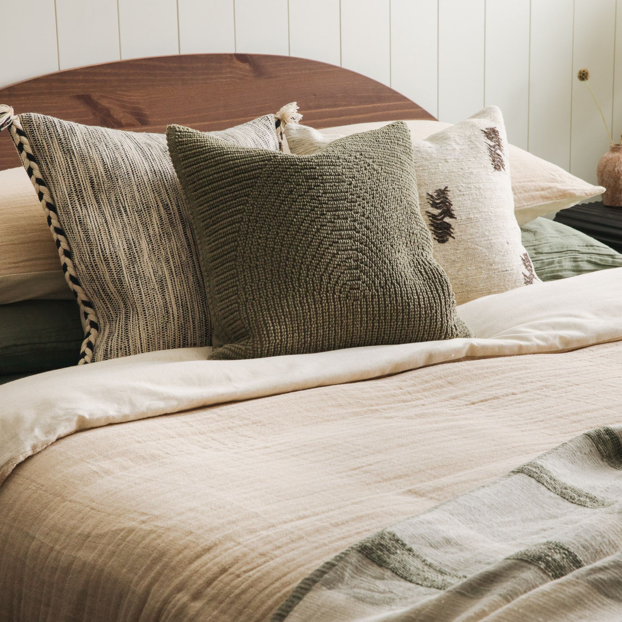 Bed with layered neutral pillows and beige bedding, set against a wood headboard