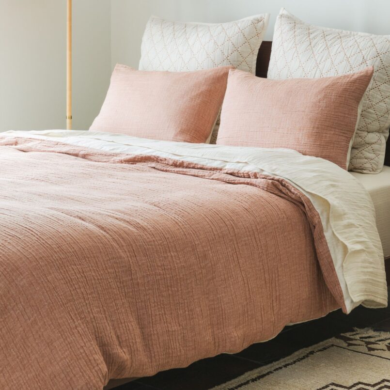 Bed with soft pink comforter and white pillows in a minimal, light-filled room