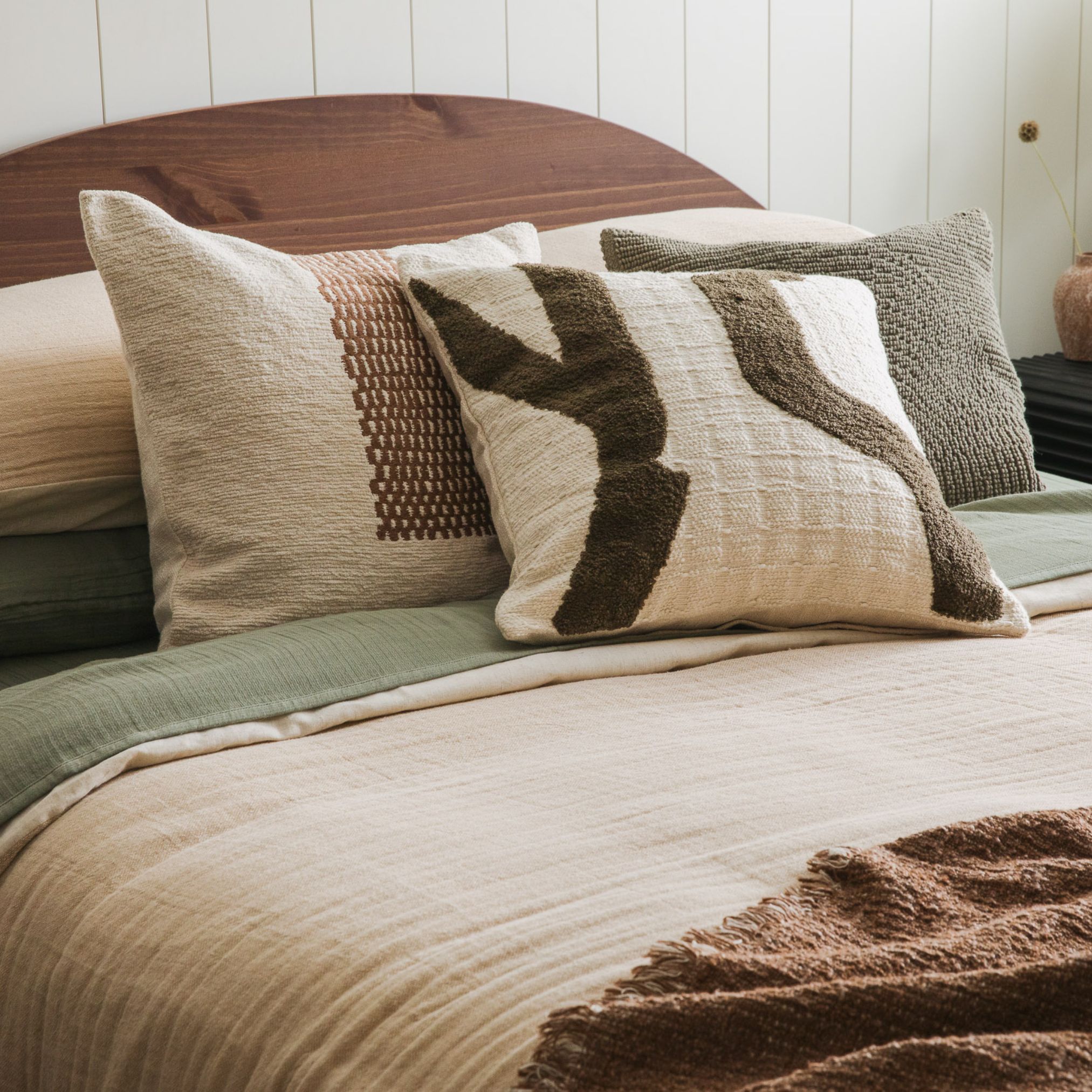 Bed with layered neutral pillows and beige bedding, set against a wood headboard