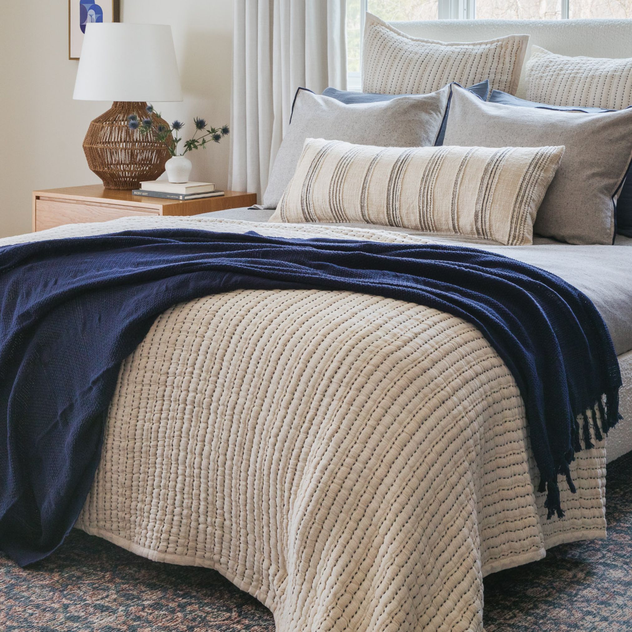 Beige knit throw blanket draped over a cream chair beside a navy headboard