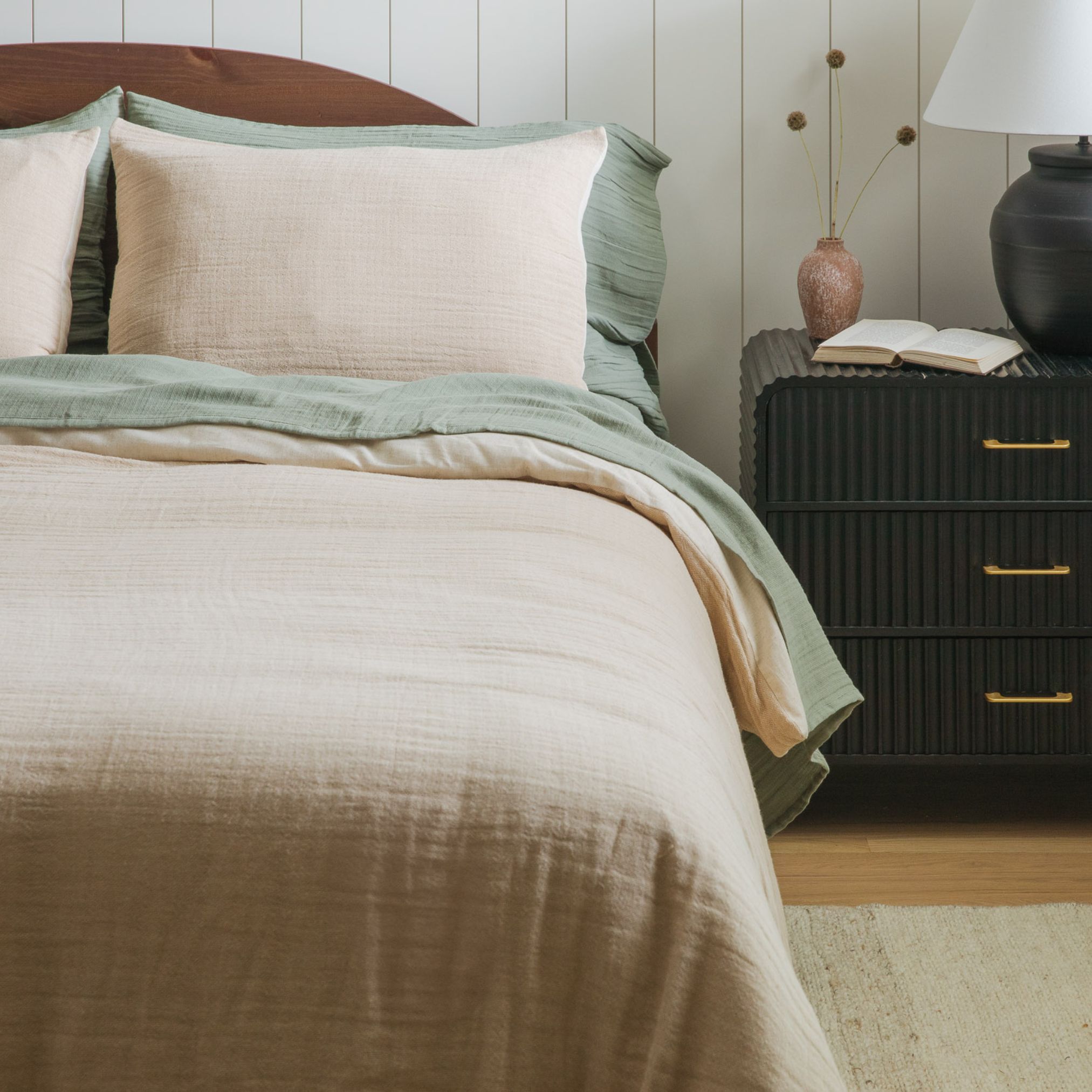 Bed with beige and white layered bedding, rust blanket, and nightstand