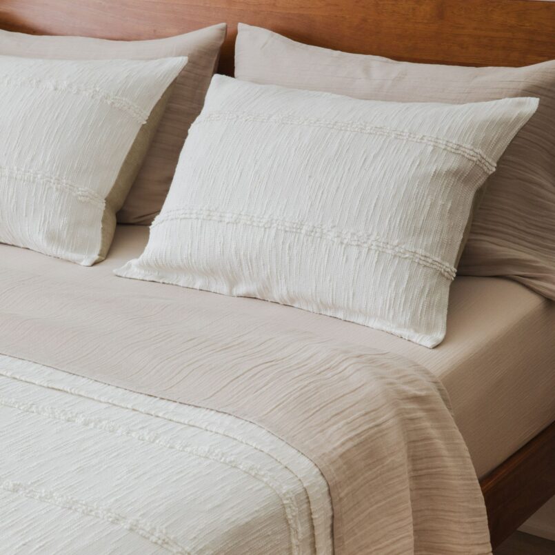 Neutral bed with beige comforter, white pillows, and light wood headboard