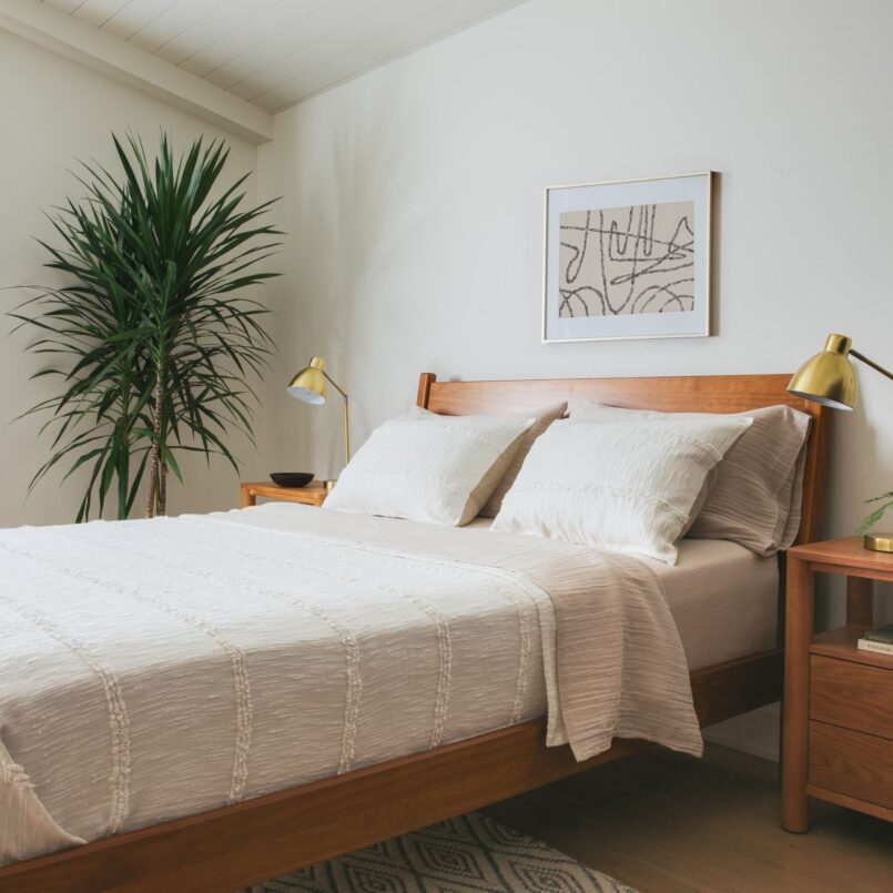 Neutral bed with beige comforter, white pillows, and light wood headboard