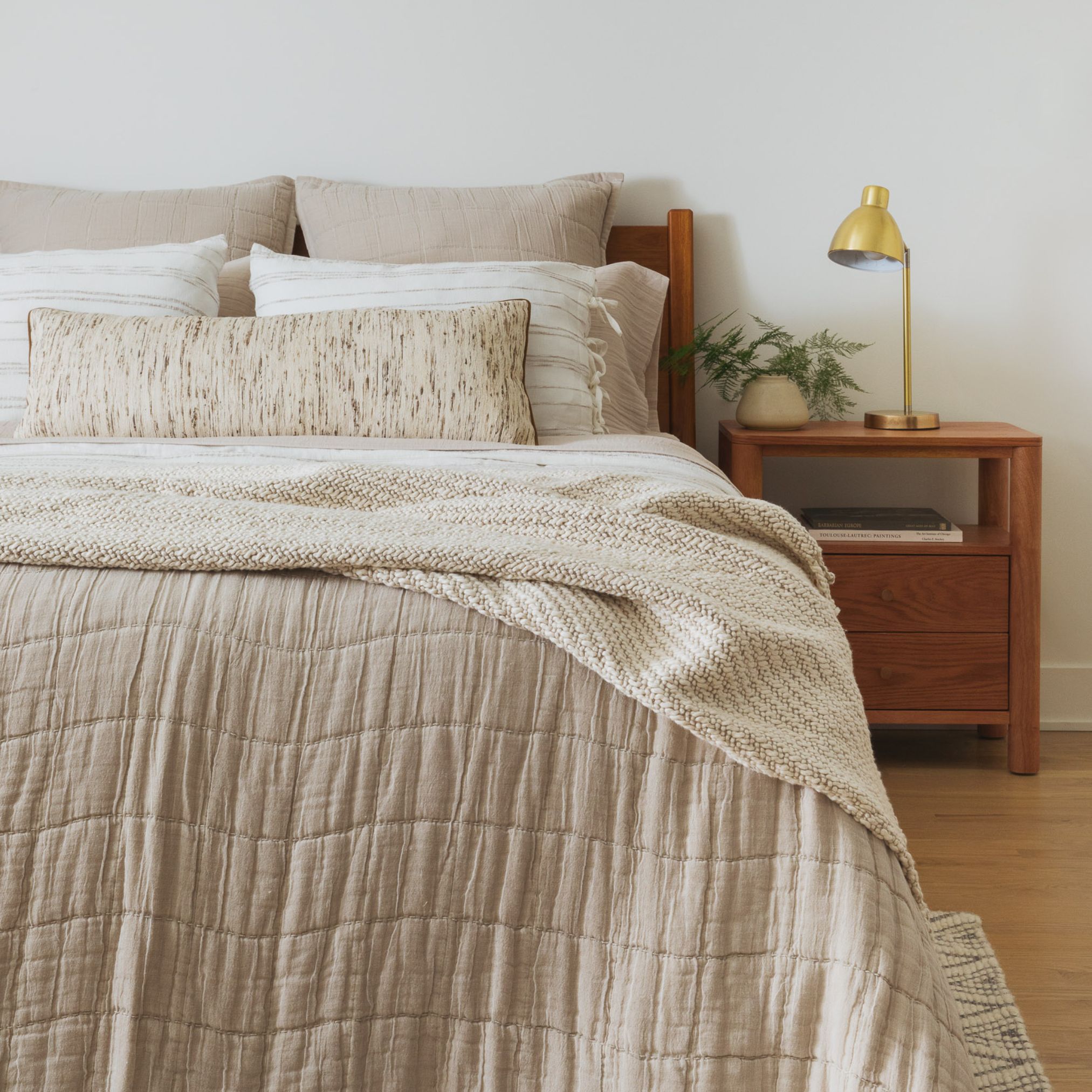 Neutral bed with beige comforter, white pillows, and light wood headboard