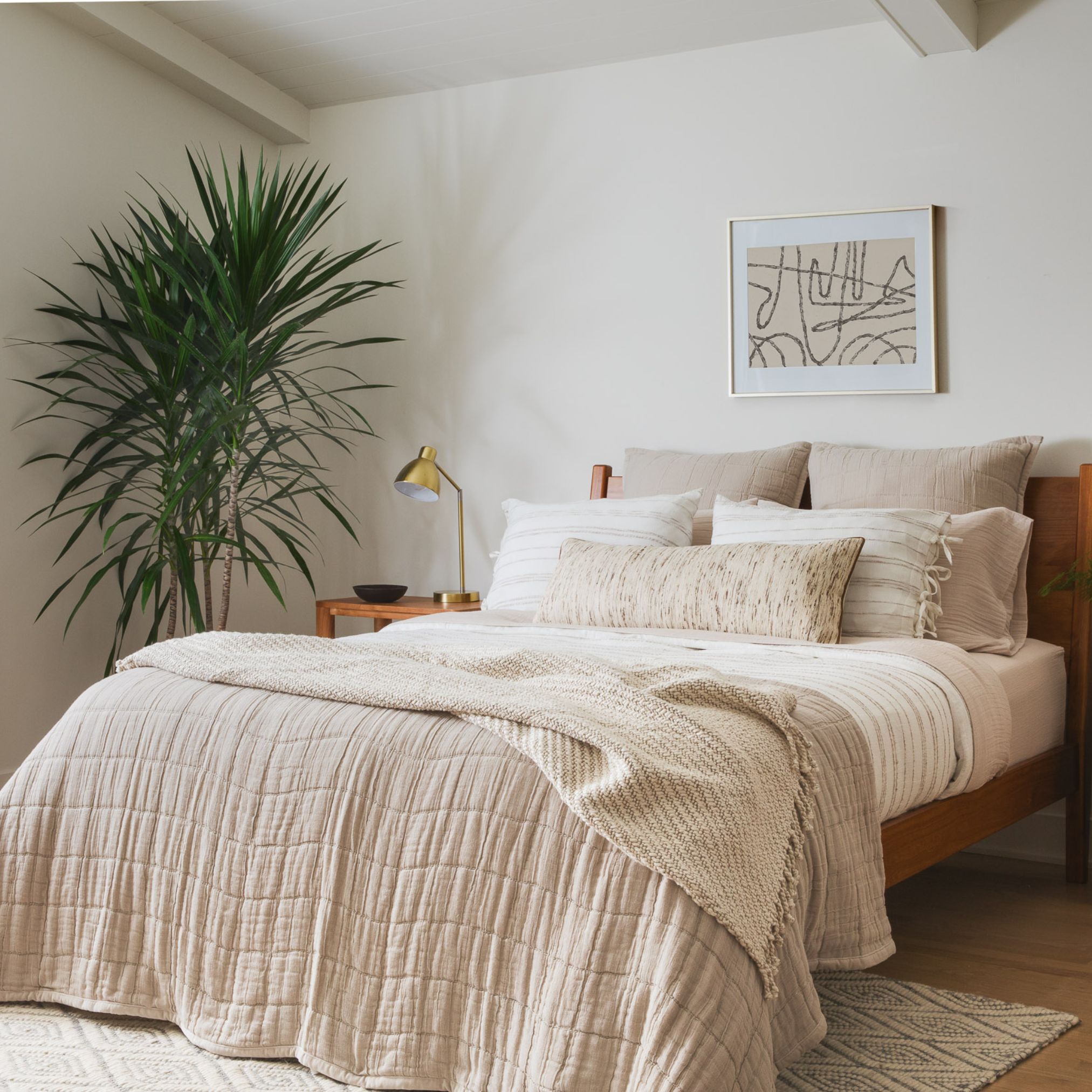 Bed with rust-colored bedding, white pillows, and a potted plant in the background