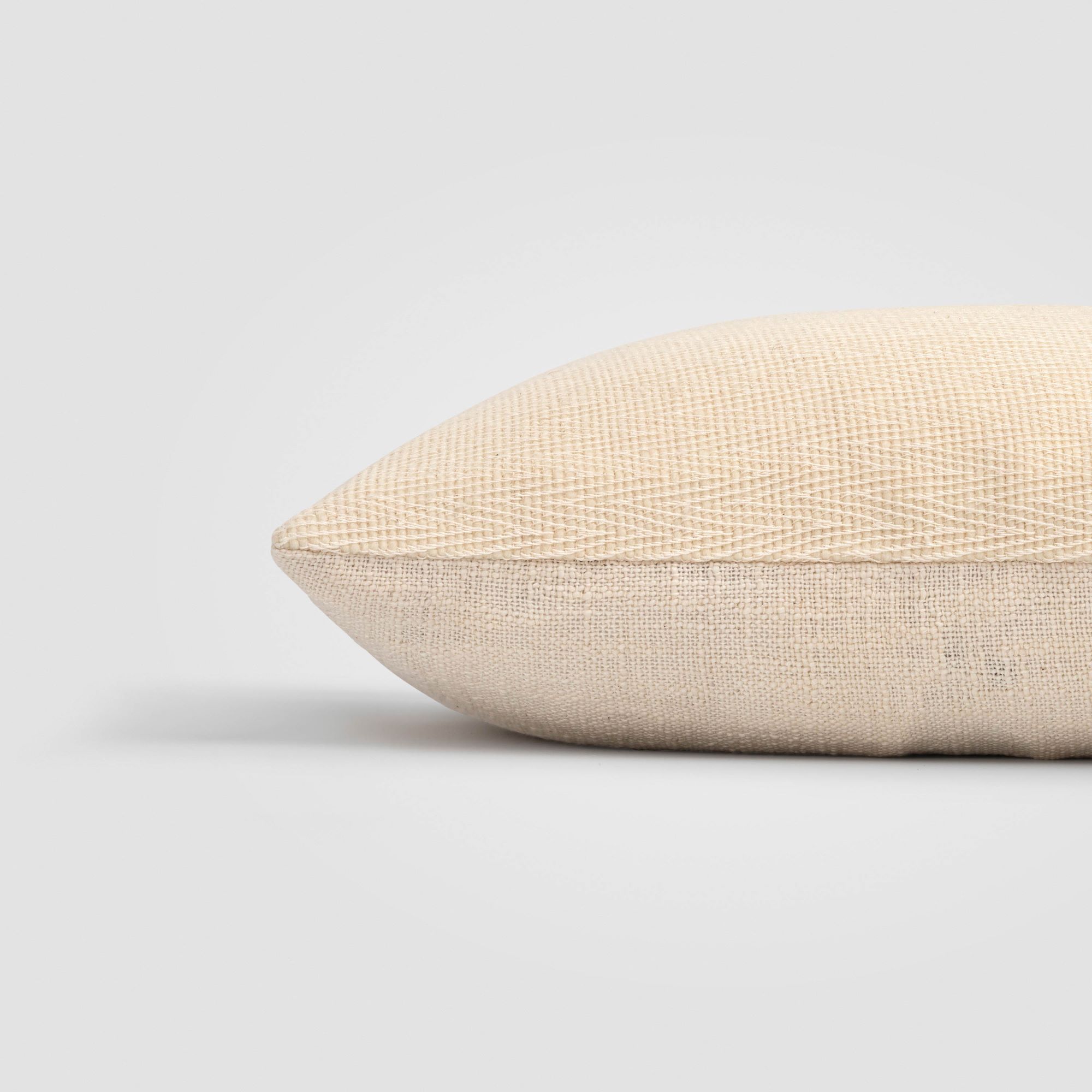 Side view of a beige pillow with fine stitching along the edge