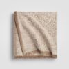 Folded beige cable knit throw blanket with a ribbed edge
