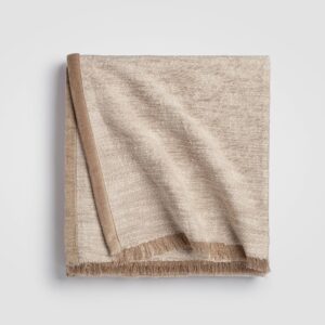 Folded beige cable knit throw blanket with a ribbed edge