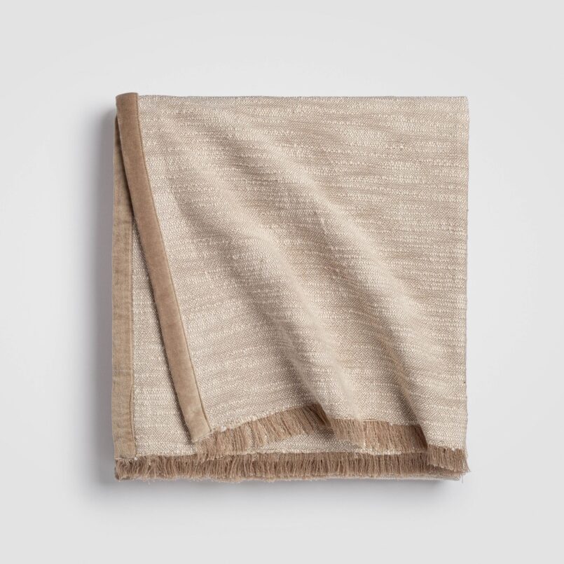 Folded beige cable knit throw blanket with a ribbed edge