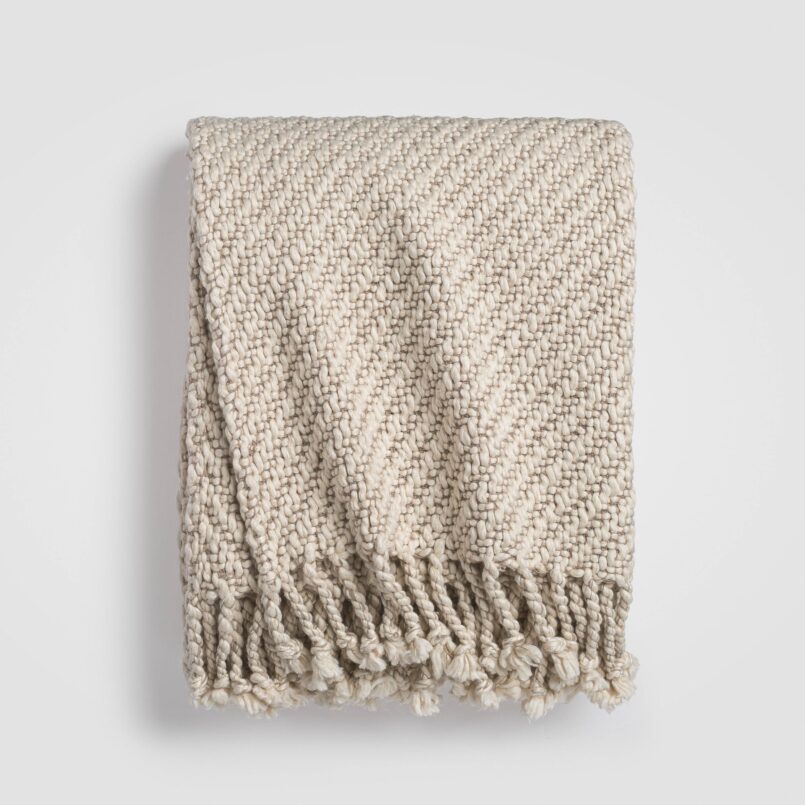 Folded beige knit throw blanket with textured stitching and soft drape