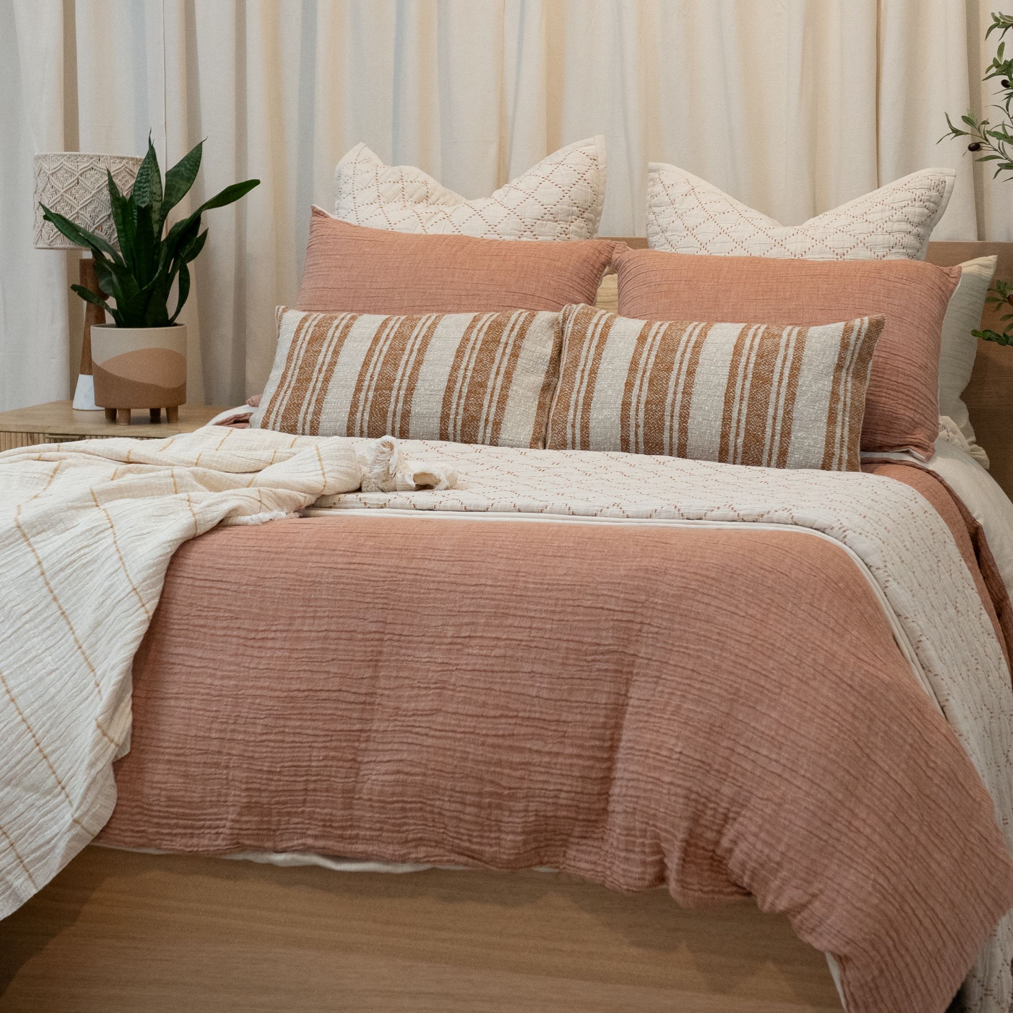 Bed with soft pink comforter, blush accent pillow, and white sheets in a bright room