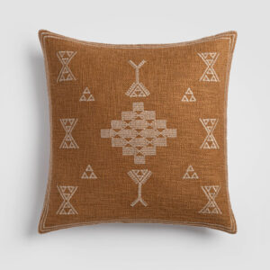 Burnt orange pillow with white tribal-inspired embroidered symbols