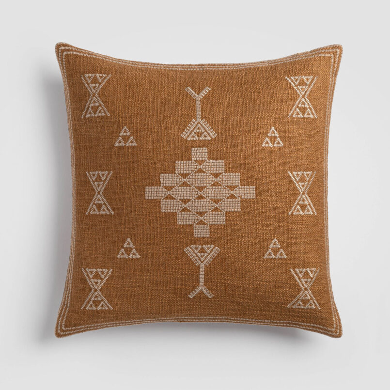 Burnt orange pillow with white tribal-inspired embroidered symbols