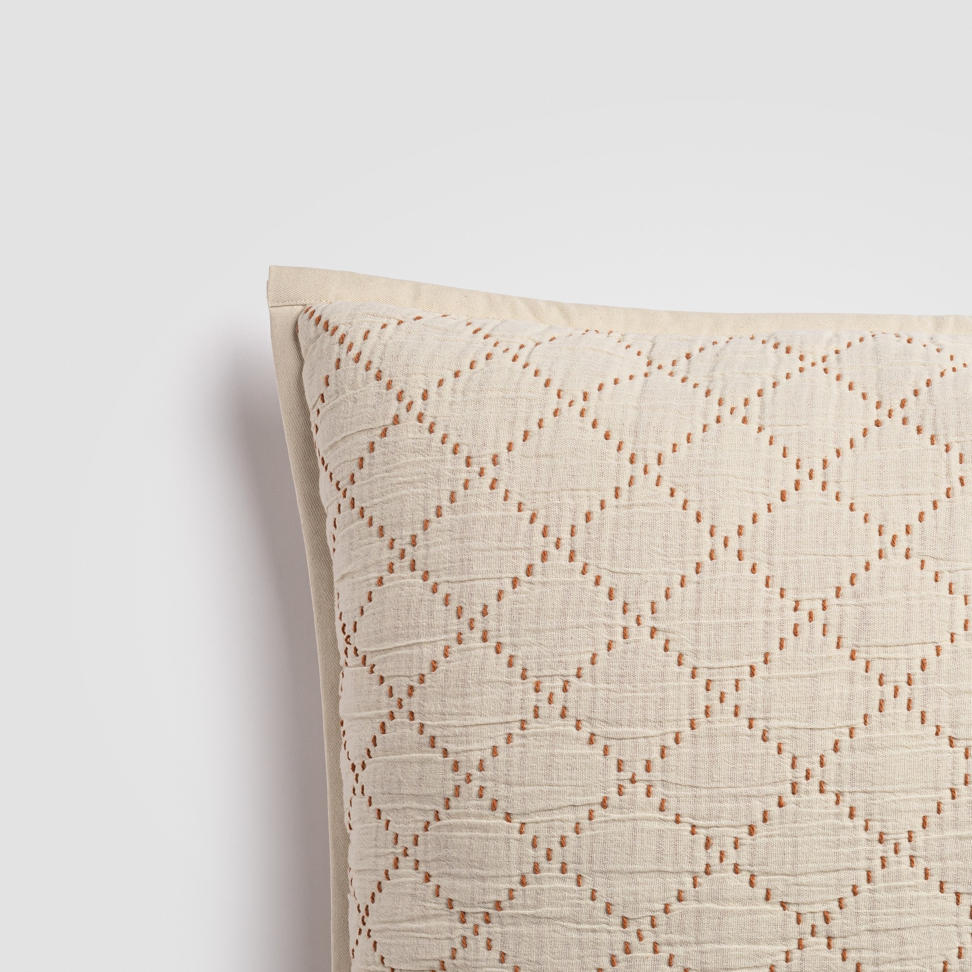 Close-up of cream pillow with textured diamond embroidery pattern