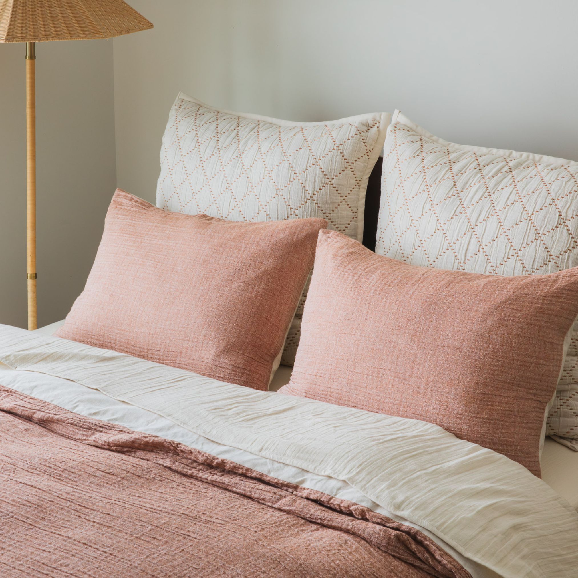 Bed with blush pink bedding and matching pillows in a softly lit bedroom