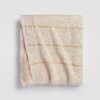 Folded beige knit throw blanket with textured stitching and soft drape