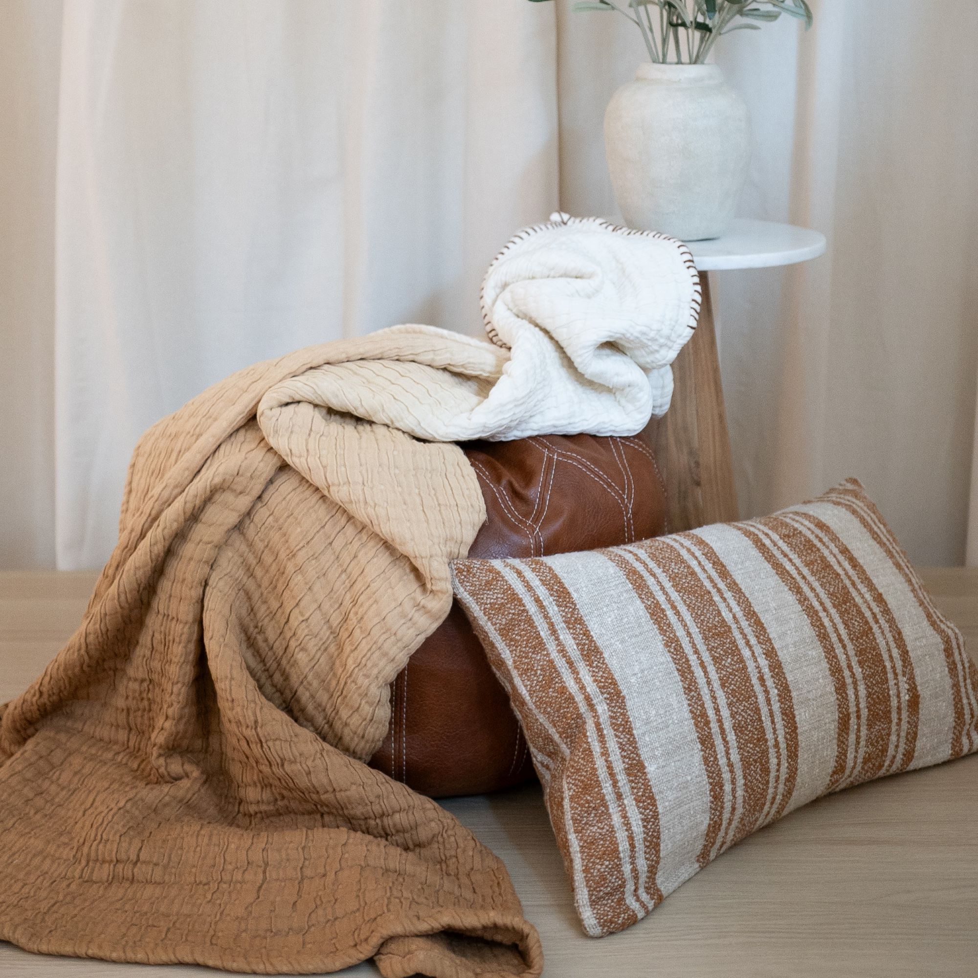 Bed with light beige bedding, striped pillowcases, and a rust-colored throw folded at the foot