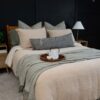 Bed styled with tan and brown decorative pillows, layered beige bedding, and a rust-colored throw