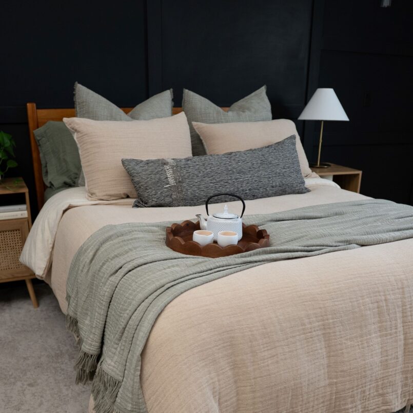 Bed styled with tan and brown decorative pillows, layered beige bedding, and a rust-colored throw