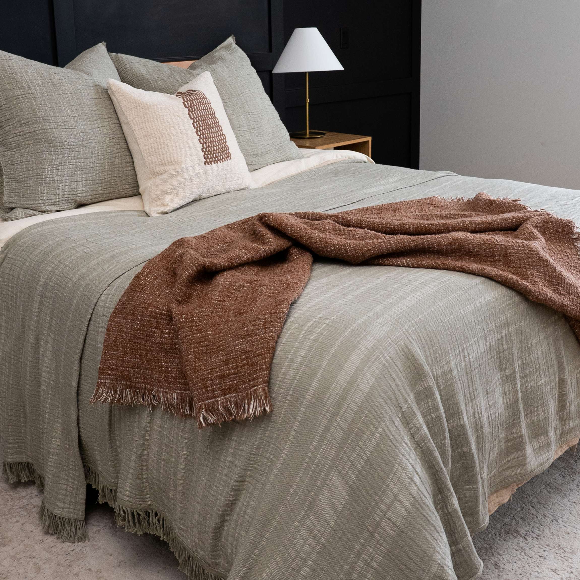 Cream-colored bedding with layered pillows and a rust blanket folded across the foot of the bed