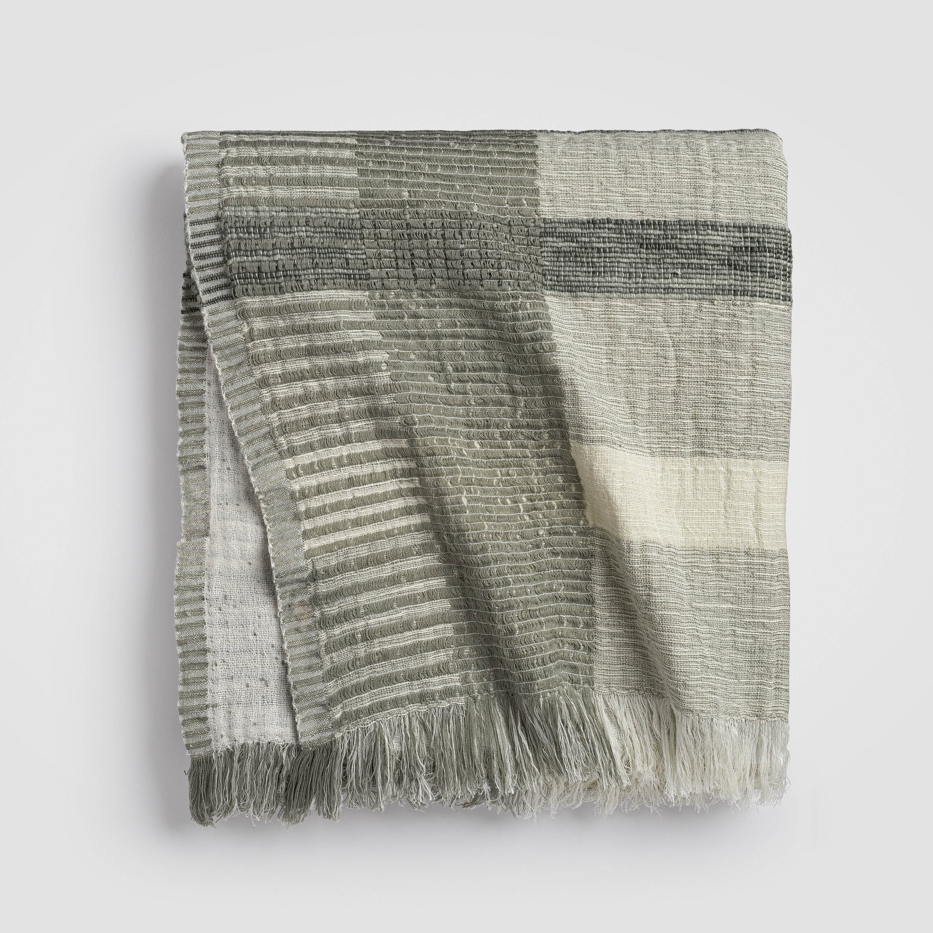 Folded striped knit blanket in green and ivory tones with a soft drape