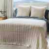 Made bed with two pale striped pillows and matching quilt in sunlit room