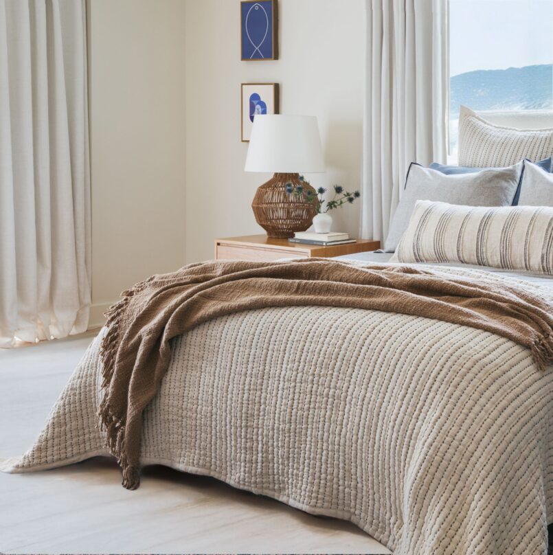 Bed with dark botanical print pillow and tan bedding in cozy bedroom setting