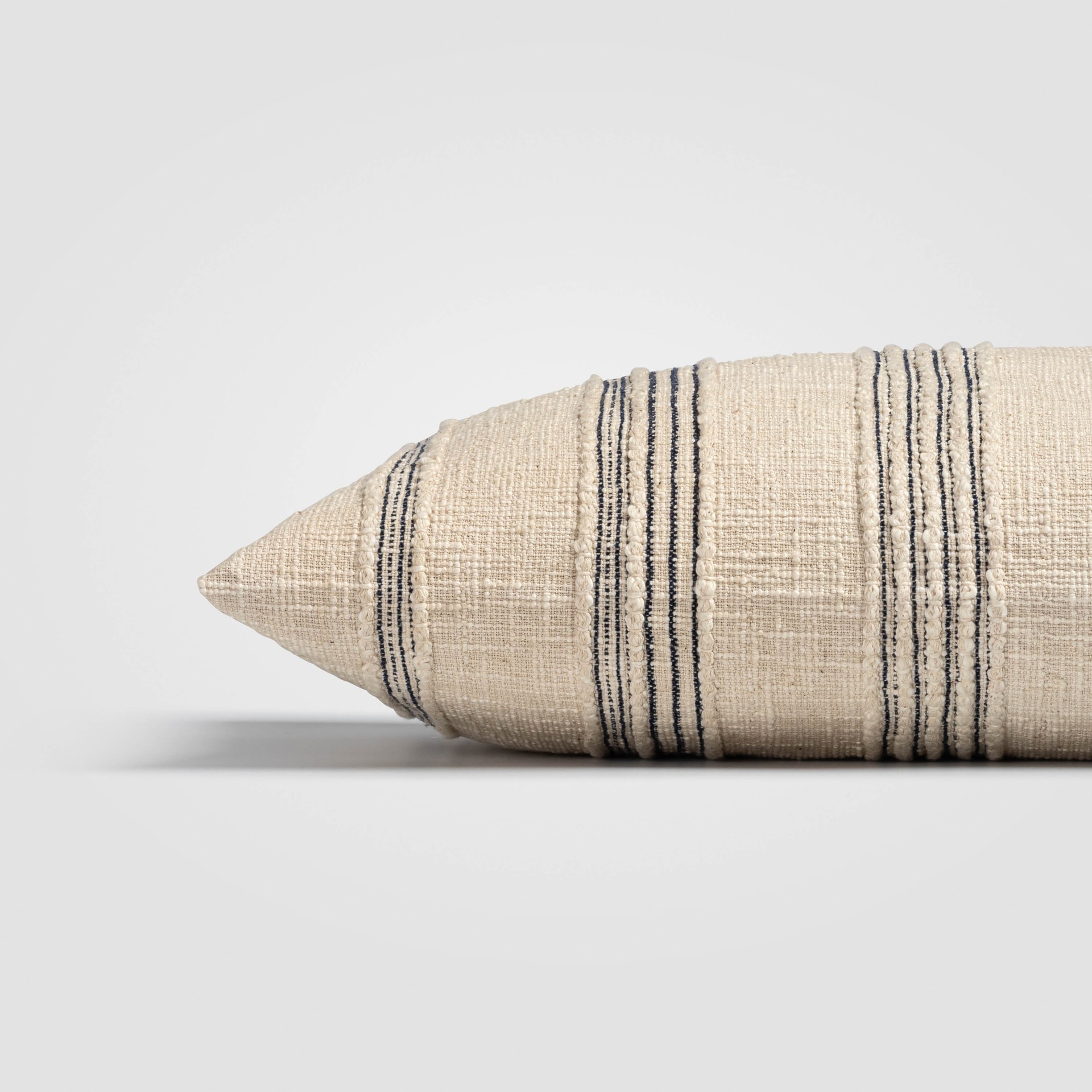 Rectangular beige pillow with horizontal stitched lines and tassels on each end