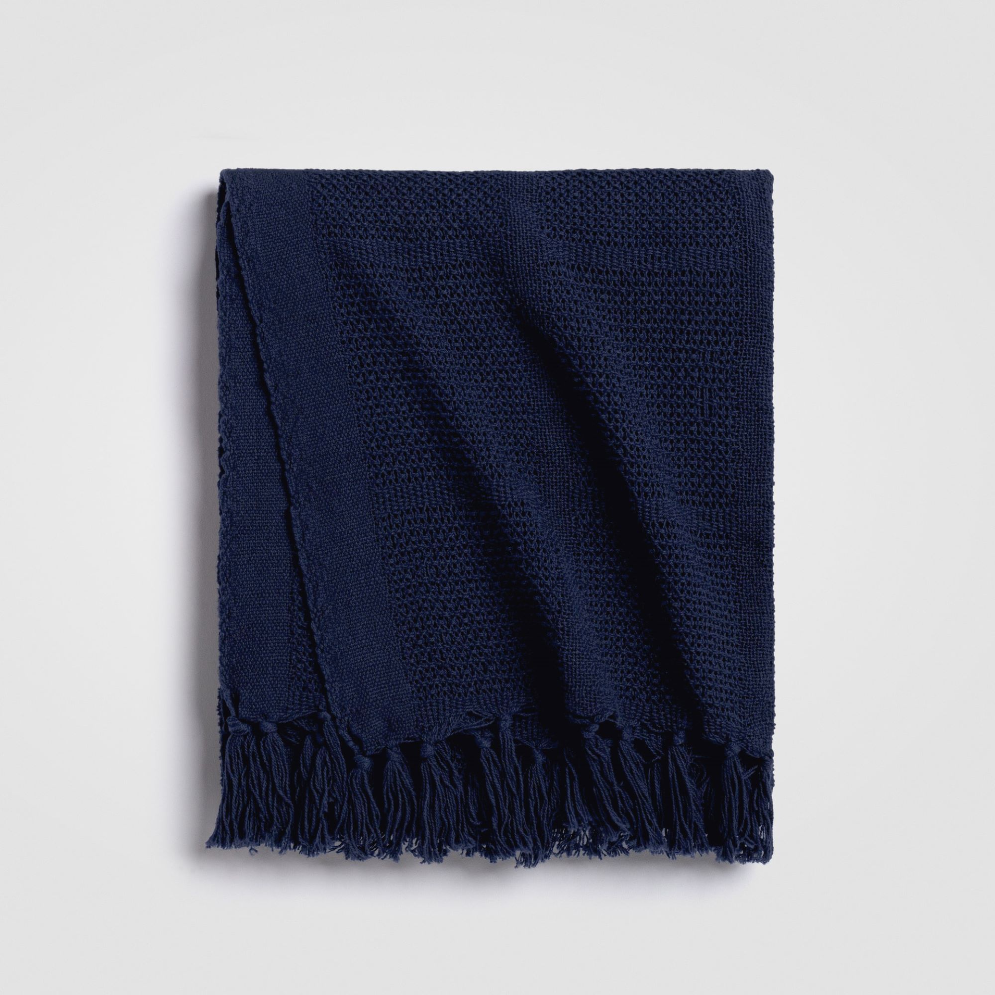 Folded dark navy throw blanket with fringe edges on a white background